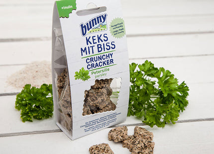 Een zakje Bunny Nature - Crunchy Cracker Peterselie hondenvoer met peterselie ernaast, voor een gezonde hap voor uw harige vriend.