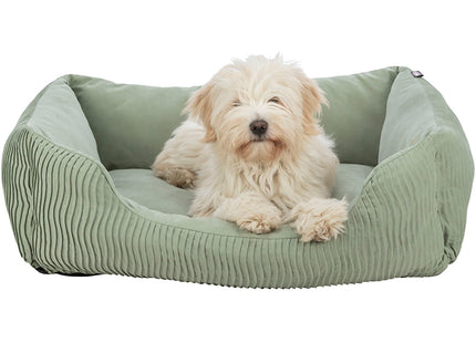 Een kleine witte hond rustend in een comfortabele Trixie - Hondenmand Marley - Soft Edition bedekt met een zachte groene katoenen hoes.