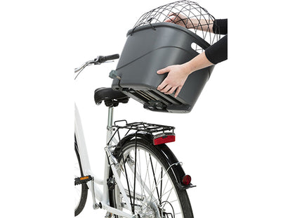 Op een fiets houdt iemand een Trixie - Kunststof Fietsmand Bagagedrager vast, voorzien van een optionele korte houder voor extra gemak en een antislipmat voor eenvoudig schoonmaken en bevestigen. De mand biedt tevens bescherming tegen rammelen en is.