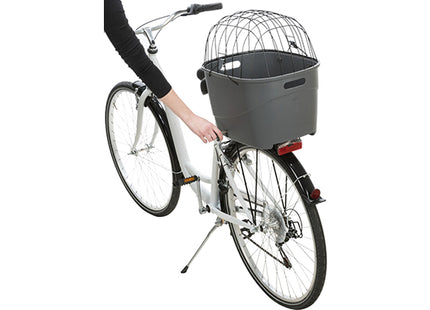 Een persoon die de Trixie - Kunststof Fietsmand Bagagedrager op de fiets vasthoudt, met antislipvloermat en eenvoudig schoon te maken opzetstuk ter bescherming tegen rammelen.
