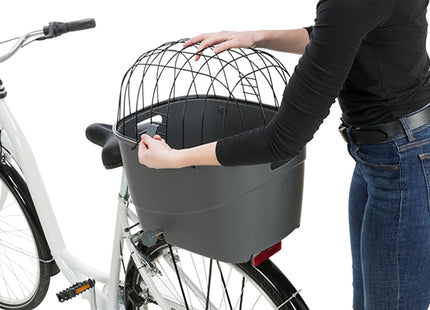 Een vrouw fietst met een Trixie - Kunststof Fietsmand Bagagedrager stevig vastgemaakt aan haar fiets.